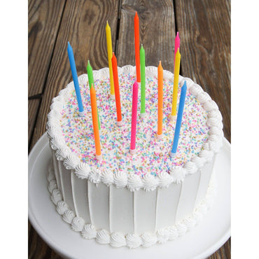 Colorful neon rainbow candles set from Party Partners, arranged on a white surface with vibrant, glowing candle lights.
